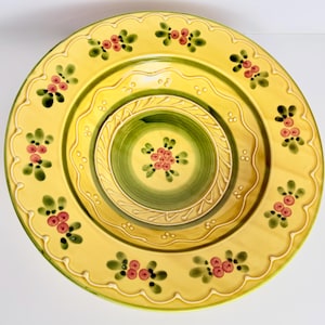Puede incluir: Un juego de tres platos decorativos de cerámica. El plato más grande es amarillo con un borde festoneado y detalles florales. El plato del medio es amarillo con un centro verde, y el más pequeño es verde con un diseño floral.