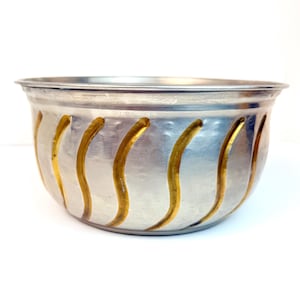 May include: A silver bowl with a wavy gold design. The bowl is round and has a smooth surface.