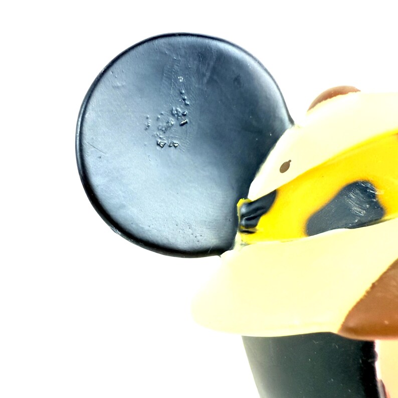 May include: Close-up of a black Mickey Mouse ear with a brown and yellow hat. The ear is made of a smooth, black material and has a small, round, brown spot on the back.