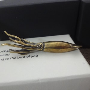 May include: A bronze-coloured squid figurine with detailed tentacles and body. The sculpture is resting on a white surface with the text "JEWEL beauty ong to the best of you".