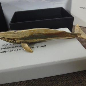 May include: A small, gold-colored whale sculpture on a white box with the text "SMALL JEWELRY unique beauty, only belong to the best of you".