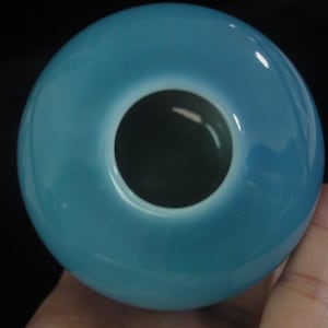 May include: A smooth, spherical ceramic vase with a glossy, vibrant turquoise blue glaze. The object features a circular opening at the top, revealing a white interior. The surface is uniform and reflective, showcasing a consistent color throughout.