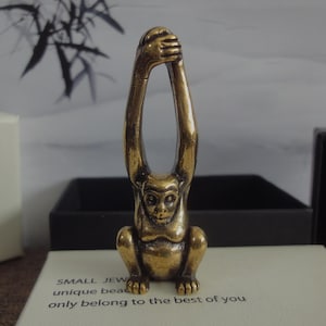 May include: A small gold-colored monkey figurine with its arms raised above its head. The monkey is sitting on a white surface with the text "SMALL JEW unique bead only belong to the best of you" visible below it.