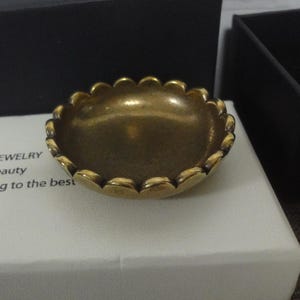 May include: A small, gold-coloured, decorative dish with a scalloped edge. The dish is made of metal and has a smooth, shiny surface.