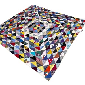 May include: A square quilt constructed from a multitude of small triangular fabric patches in a wide variety of colors, including red, yellow, blue, green, black, and white, featuring diverse patterns such as polka dots, stripes, and plaids.