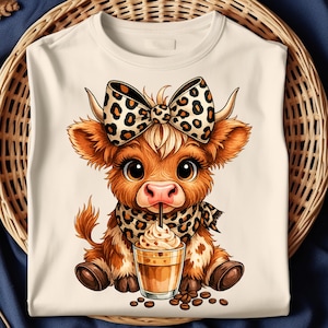 Puede incluir: Camiseta color crema con una vaca de dibujos animados con un lazo con estampado de leopardo, una bufanda y una bebida de caf&eacute;. La vaca es marr&oacute;n con ojos grandes y est&aacute; sentada. Los granos de caf&eacute; est&aacute;n esparcidos alrededor de la bebida.