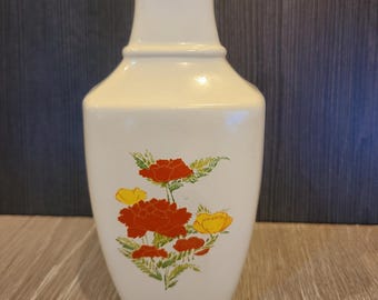 May include: A cream-colored ceramic vase with a flared top and a wide base. The vase features a floral design with red and yellow flowers and green leaves. The vase is approximately 10 inches tall.