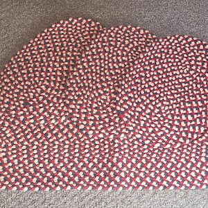May include: A large, round braided rug with a red, white, and blue pattern. The rug is made of thick, woven rope and has a textured surface.