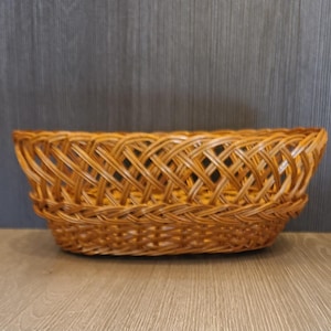 May include: A woven wicker basket with a rectangular shape. The basket is made of light brown wicker and has a tightly woven pattern. The basket is empty and sits on a wooden surface.