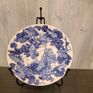 May include: A white ceramic plate with a blue and white grapevine design. The plate is on a black metal stand.