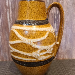 May include: A vintage ceramic pitcher with a handle, featuring a textured brown surface with black and white decorative bands. The pitcher has a cylindrical top and a rounded body, suitable for serving beverages.