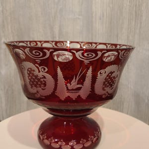 May include: A ruby red glass bowl with a white etched design of birds and floral patterns. The bowl has a footed base.