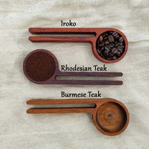 May include: Three wooden scoops with different wood types labeled: Iroko, Rhodesian Teak, and Burmese Teak. The scoops are filled with coffee beans and grounds.