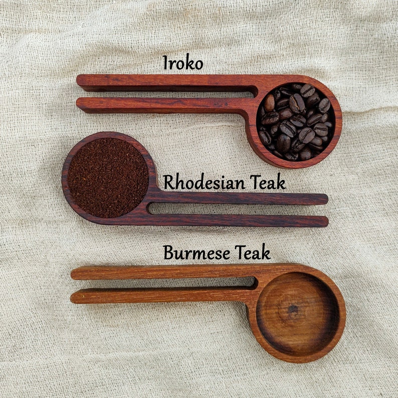 May include: Three wooden scoops with different wood types labeled: Iroko, Rhodesian Teak, and Burmese Teak. The scoops are filled with coffee beans and grounds.
