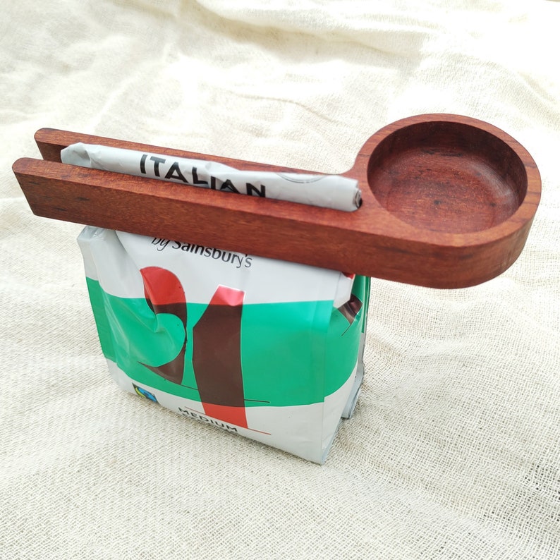 May include: A wooden scoop with a handle and a round bowl, used for scooping coffee beans. The scoop is resting on top of a bag of "Italian" coffee beans by Sainsbury's.