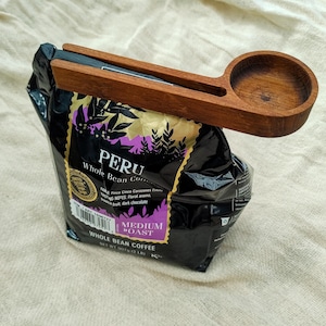 May include: A wooden coffee bag clip with a scoop. The bag is labeled "Peru Whole Bean Coffee" and features a medium roast. The bag is 2 pounds.