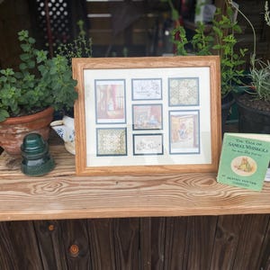 May include: A wooden framed artwork with six small illustrations, a vintage book titled "The Tale of Samuel Whiskers", and potted plants on a wooden shelf. The book has a green cover with a circular illustration. A green glass insulator sits on the shelf.