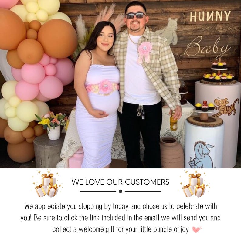May include: A pregnant woman and a man stand in front of a wooden sign that says "Hunny Baby". The woman is wearing a white dress with a pink flower sash. The man is wearing a plaid shirt and a pink ribbon. There are balloons and decorations in the background.