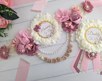 Könnte beinhalten: Eine Sammlung von Babyparty-Dekorationen in Rosa-, Creme- und Mauve-Tönen. Das Set beinhaltet florale Verzierungen, Bänder und eine Holzkette mit dem Schriftzug "BABY NAME". Die Artikel sind für "Mommy To Be" und "Daddy To Be" gedacht.