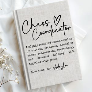 May include: A hardcover journal with the words "Chaos Coordinator" in black script, with a heart symbol. The journal's cover also includes text describing the role of a chaos coordinator and the name "Adeyln".
