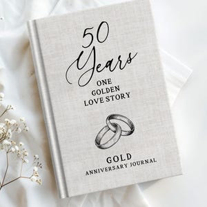 May include: A light-colored journal with the text "50 Years One Golden Love Story" and "Gold Anniversary Journal" in black script. The cover features an illustration of two intertwined rings. The journal is on a white surface.