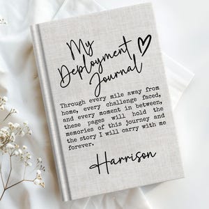 May include: A light gray fabric-covered journal with black text that reads My Deployment Journal, a heart symbol, a paragraph about memories of a journey, and the name Harrison printed in a script font on the front cover.