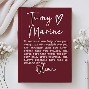 May include: A deep red hardcover journal featuring white text that reads: To my Marine, No matter where duty takes you, carry this with confidence: you are stronger than you know, braver than you realize, and loved more than words can say. Stay safe, trust yourself, and always remember that home is waiting for you. Olivia.