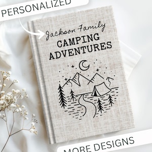 May include: A personalized journal with the text "Jackson Family CAMPING ADVENTURES" in black. The cover features a black and white illustration of mountains, trees, a tent, and a crescent moon. The journal is light beige and has the word "PERSONALIZED" at the top.