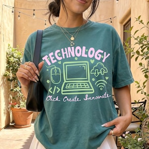 May include: A dark teal short-sleeve t-shirt featuring the word TECHNOLOGY in pink, with a light green graphic of a laptop, computer mouse, and cloud icon. Below the graphic, the text reads Click. Create. Innovate. in pink cursive script.