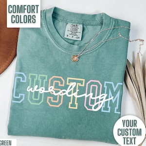 May include: Light green t-shirt with the text "CUSTOM wording" in rainbow colors. The shirt is made of a soft, comfortable material and has a relaxed fit.