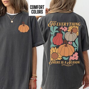 May include: A dark gray t-shirt with a pumpkin graphic on the front and a graphic on the back that says "To Everything There Is A Season Ecclesiastes 3:1" with pumpkins, sunflowers, and other floral elements.
