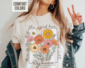 May include: White t-shirt with a floral design and the text "This is the day the Lord has made we will rejoice and be glad in it. Psalm 118:24"