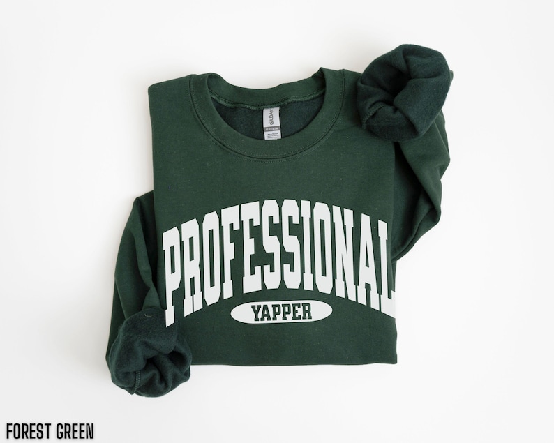 May include: Forest green sweatshirt with the text "PROFESSIONAL YAPPER" in white block letters. The sweatshirt is folded, with the sleeves bunched up. The text "FOREST GREEN" is at the bottom.