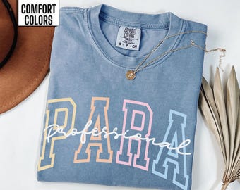 May include: A blue jean t-shirt with the word "PARA" in rainbow colors and the word "professional" written in white script underneath. The shirt is made by Comfort Colors.