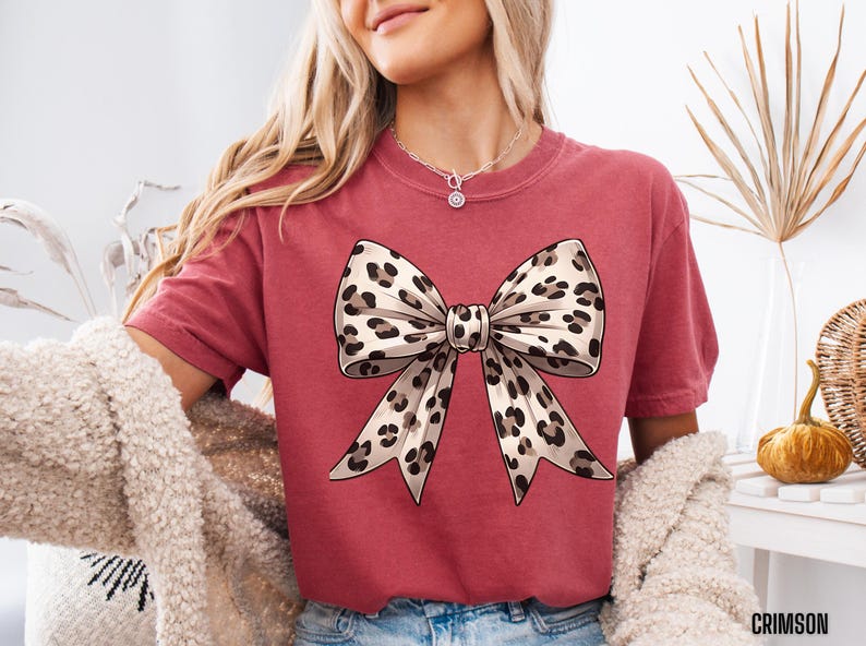 Puede incluir: Una camiseta roja con un gran lazo de estampado de leopardo marr&oacute;n y blanco en la parte delantera.