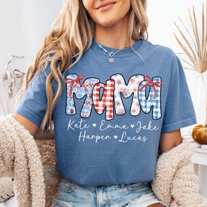 May include: Blue jean colored t-shirt with the word "MAMA" in a patriotic design. The letters are decorated with red gingham, blue gingham, and firework patterns. Below the word "MAMA" are the names Kate, Emma, Jake, Harper, and Lucas.