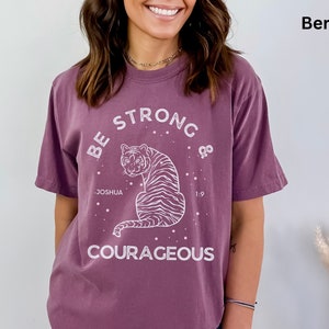 May include: A purple t-shirt with a white graphic of a tiger and the text "Be Strong & Courageous" with the words "Joshua 1:9" underneath the tiger.