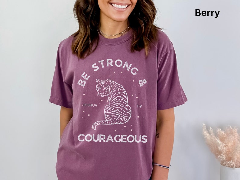 May include: A purple t-shirt with a white graphic of a tiger and the text "Be Strong & Courageous" with the words "Joshua 1:9" underneath the tiger.