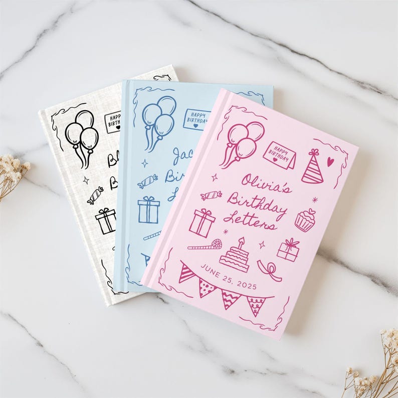 May include: Three personalized birthday journals in white, light blue, and pink. Each journal features hand-drawn illustrations of balloons, gifts, and a cake. The pink journal is labeled "Olivia's Birthday Letters" with a date of June 25, 2025.