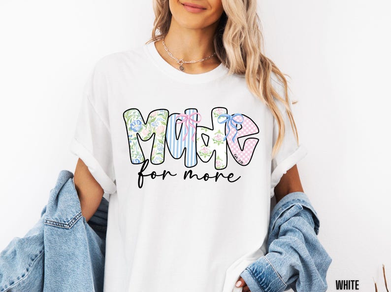 Op de afbeelding: Wit T-shirt met de tekst "MADE for more" in een kleurrijk ontwerp met bloemen- en streepmotieven. Het T-shirt heeft een relaxte pasvorm.
