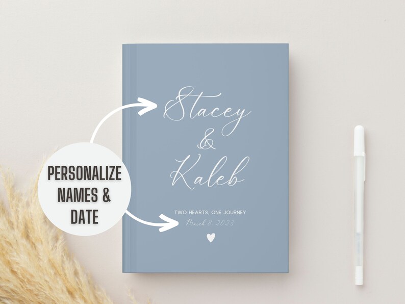 K&ouml;nnte beinhalten: Ein hellblaues Journal mit dem Text "Stacey & Kaleb" in wei&szlig;er Kursivschrift. Der Text "Two Hearts, One Journey" und das Datum "March 9, 2023" sind ebenfalls in wei&szlig;er Kursivschrift.