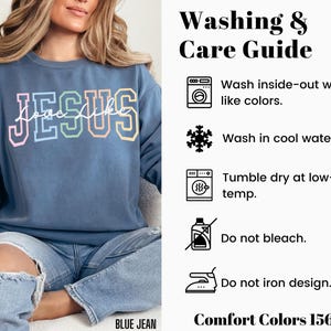 May include: A blue sweatshirt with the text "Love Like Jesus" in rainbow colours. The image includes a washing and care guide with instructions for washing inside out, washing in cool water, tumble drying at low temperature, not bleaching, and not ironing the design. The text "Comfort Colors 1566" is also included.