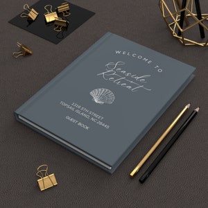 May include: A grey guest book with the text "Welcome to Seaside Retreat" and "1316 5th Street Topsail Island, NC 28445 Guest Book". A seashell illustration is on the cover.
