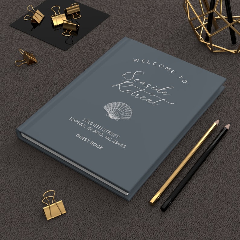May include: A grey guest book with the text "Welcome to Seaside Retreat" and "1316 5th Street Topsail Island, NC 28445 Guest Book". A seashell illustration is on the cover.