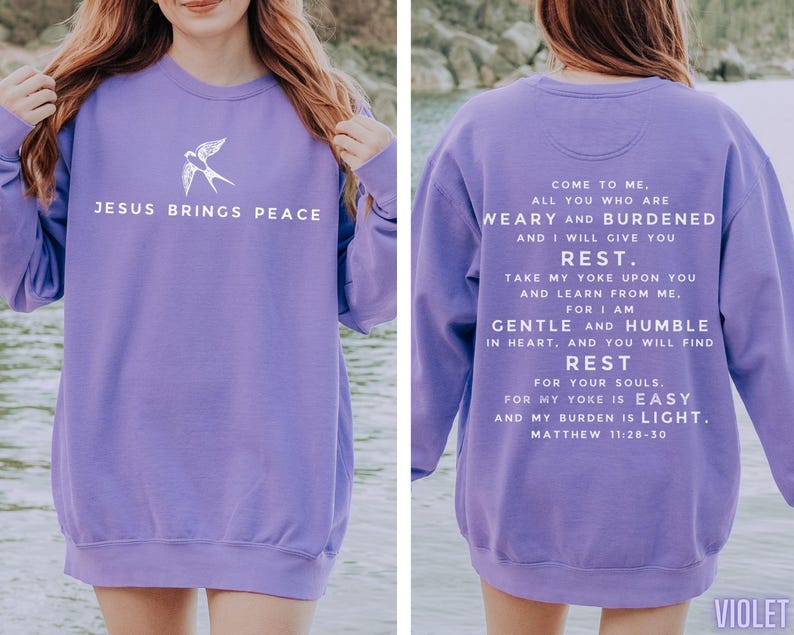 May include: Purple sweatshirt with a white bird graphic on the front and a white text quote from the Bible on the back. The quote reads "Come to me, all you who are weary and burdened, and I will give you rest. Take my yoke upon you and learn from me, for I am gentle and humble in heart, and you will find rest for your souls. For my yoke is easy and my burden is light. Matthew 11:28-30".