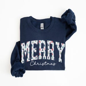 May include: A navy blue sweatshirt with a white "Merry Christmas" graphic featuring a pattern of colorful Christmas trees.