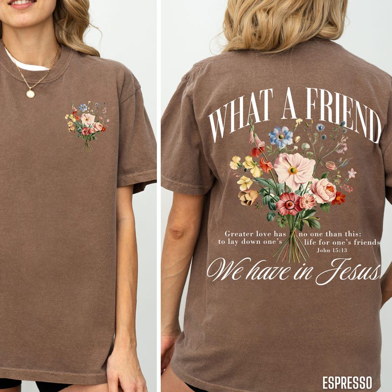 K&ouml;nnte beinhalten: Espressofarbenes T-Shirt mit einem Blumengesteck-Design auf der Vorder- und R&uuml;ckseite. Auf der R&uuml;ckseite des Shirts befindet sich der Text "WHAT A FRIEND" &uuml;ber dem Blumendesign, mit einem Bibelvers darunter. Das Shirt ist kurz&auml;rmlig und hat einen l&auml;ssigen Stil.