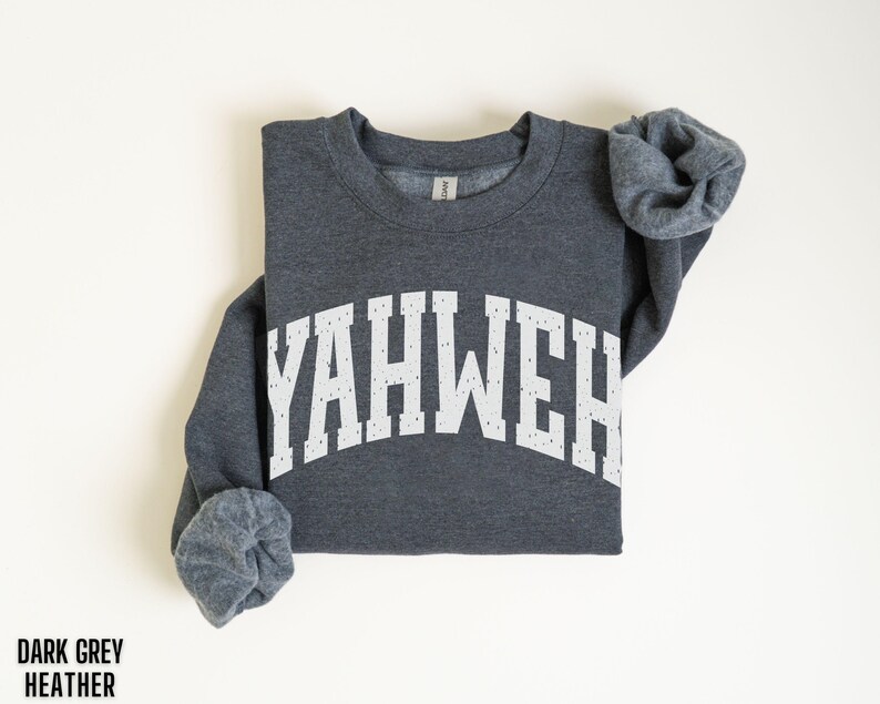 May include: Dark grey heather sweatshirt with the word "YAHWEH" printed in white, arched across the chest. The sleeves are rolled up. The words "DARK GREY HEATHER" are printed in black at the bottom left.