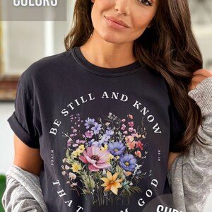 May include: Black t-shirt with a floral design and the text "Be still and know that I am God" with the reference "Psalm 46:10". The shirt is labeled "Comfort Colors" and "Super Soft".
