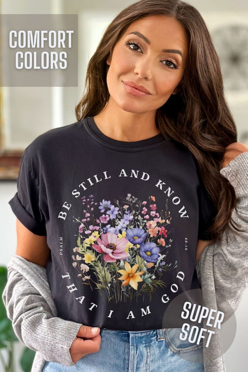 May include: Black t-shirt with a floral design and the text "Be still and know that I am God" with the reference "Psalm 46:10". The shirt is labeled "Comfort Colors" and "Super Soft".